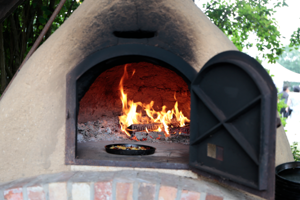KI generiert: Ein gemauerter Pizzaofen mit offener Tür, darin brennt ein Feuer.