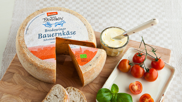 KI generiert: Ein Käselaib, aufgeschnitten mit Brot, Butter und Kirschtomaten. Text: "Brodowiner Bauernkäse."