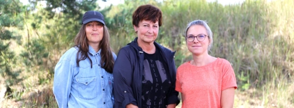 KI generiert: Drei Personen stehen draußen vor einer grünen, grasbewachsenen Kulisse.