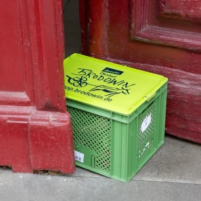 KI generiert: Grüne Kiste mit gelbem Deckel vor roter Tür. Text: "Brodowin, www.brodowin.de".