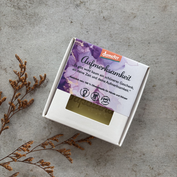 KI generiert: Eine Olivenseife in einer Box mit dem Text: „Aufmerksamkeit. Natürlich rein. 100 % Olivenseife für Hände und Körper.“