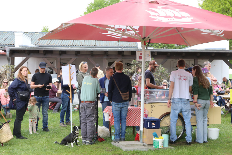 KI generiert: Eine Gruppe von Menschen unter einem roten Sonnenschirm auf einem Markt oder Fest im Freien.