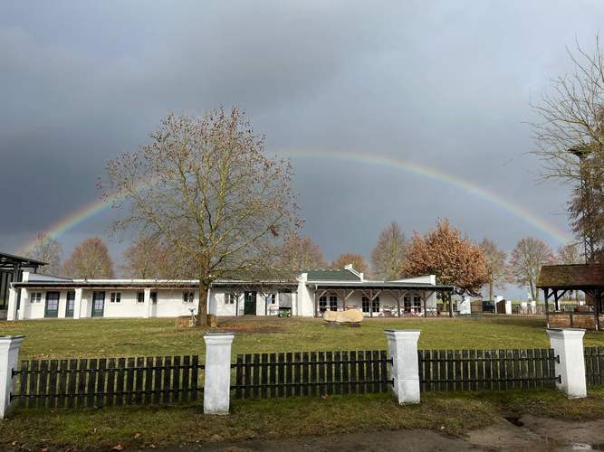 KI generiert: Ein Regenbogen über einem Gebäude mit säulenartigem Zaun im Vordergrund.