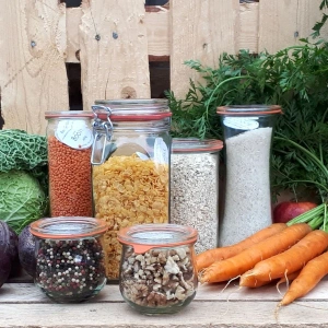 KI generiert: Ein Mann steht in einem Gewächshaus und hält eine Kiste voller Gurken. Um ihn herum befinden sich üppige Gurkenpflanzen.