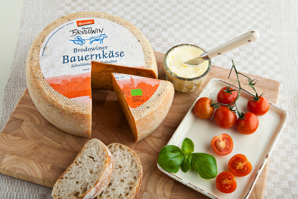 KI generiert: Ein Laib Brodowiner Bauernkäse mit Tomaten, Basilikum und Brot auf einem Holzbrett. Text: "Brodowiner Bauernkäse".