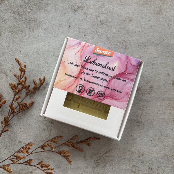 KI generiert: Eine Seifenverpackung mit dem Text "Lebenslust" und Spruch. 100% Olivenölseife für Hände und Körper.