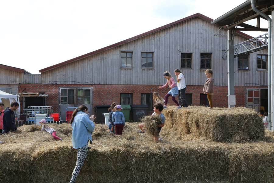 KI generiert: Kinder spielen auf Strohballen vor einem Bauernhofgebäude.