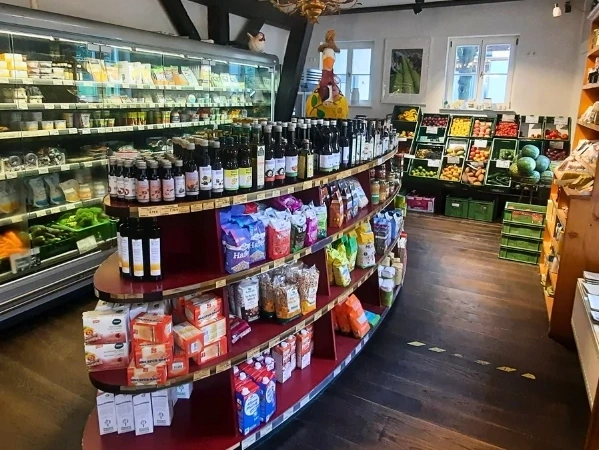 KI generiert: Das Bild zeigt eine lächelnde Frau in einem grünen Polo-Shirt, die neben einer Kiste mit frischem Gemüse steht. Der Hauptinhalt ist die Präsentation von frischen Lebensmitteln in einem möglicherweise landwirtschaftlichen oder Lagerumfeld.