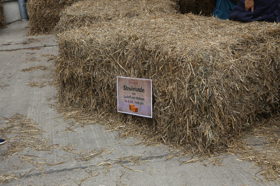 KI generiert: Strohballen mit einem Schild für eine "Strohrunde mit Ludolf von Malzahn" am Samstag um 14:00 Uhr.