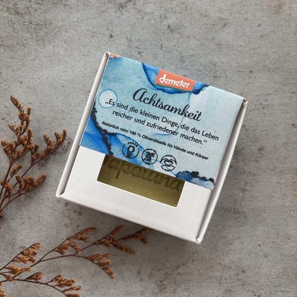 KI generiert: Eine Verpackung für Olivenölseife von Demeter, dekoriert mit getrockneten Zweigen. Text: "Achtsamkeit..."