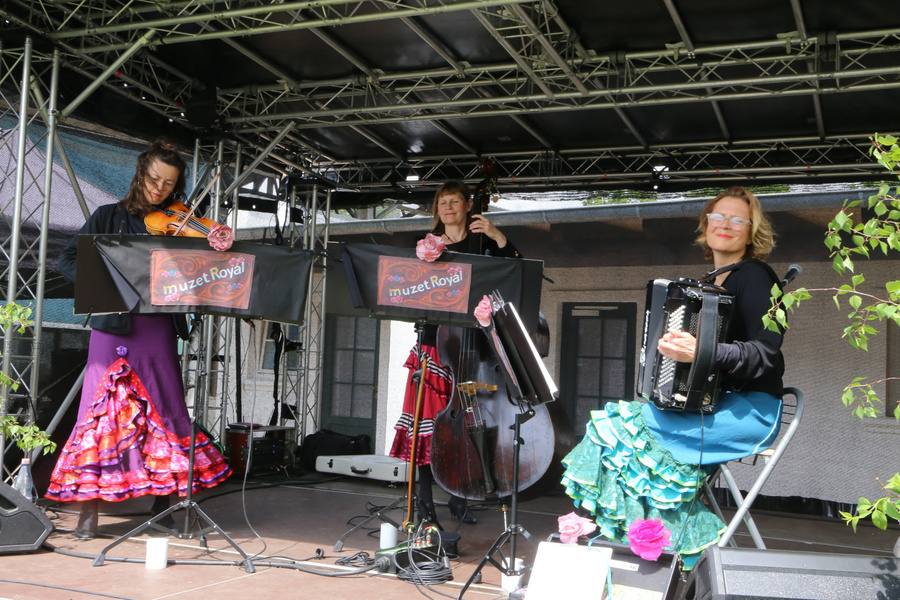 KI generiert: Drei Musikerinnen spielen auf einer Bühne. Text: „muzet Royal“.