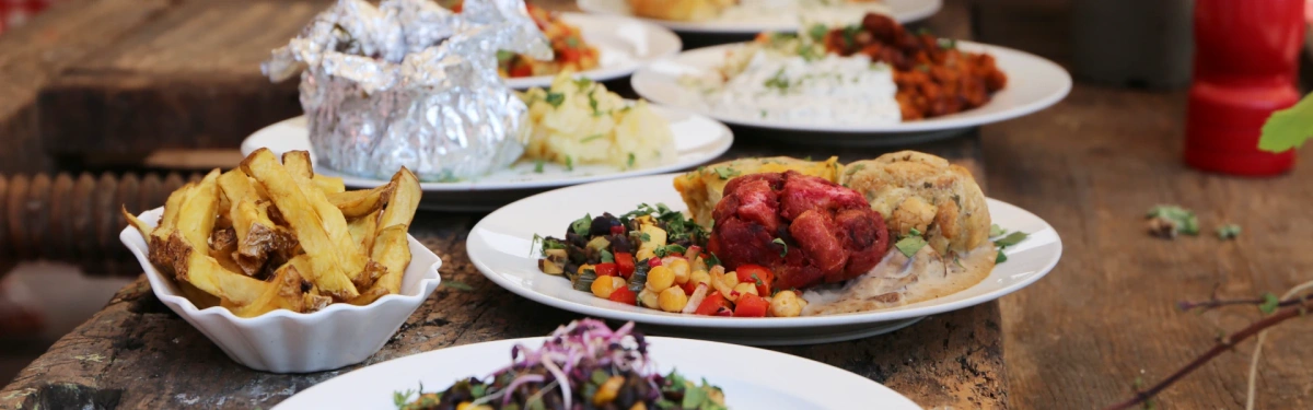 KI generiert: Eine Auswahl an bunten Gerichten auf weißen Tellern auf einem Holztisch.