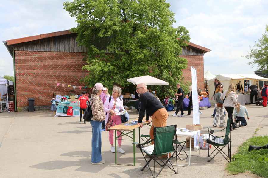 KI generiert: Ein Markt im Freien mit Menschen, Ständen und einem Baum im Hintergrund. Keine Texte erkennbar.