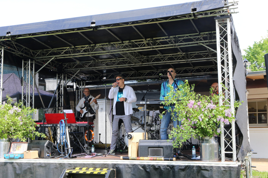 KI generiert: Eine Band spielt auf einer Bühne im Freien, umgeben von Pflanzen.
