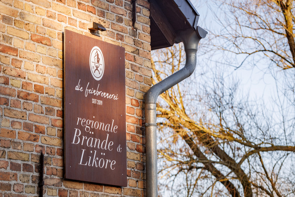 KI generiert: Schild an einer Backsteinwand: "die feinbrennerei seit 2019 regionale Brände & Liköre".